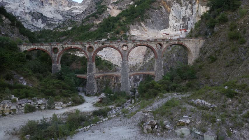Aerial view of the historic stone railway bridge surrounded by the rugged marble quarries of Carrara, Tuscany, Italy.
