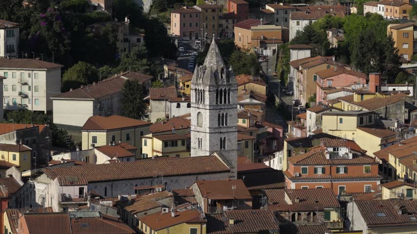 Aerial view of the historic Duomo di Carrara bell tower rising above the dense terracotta rooftops of the city in Carrara, Tuscany, Italy.