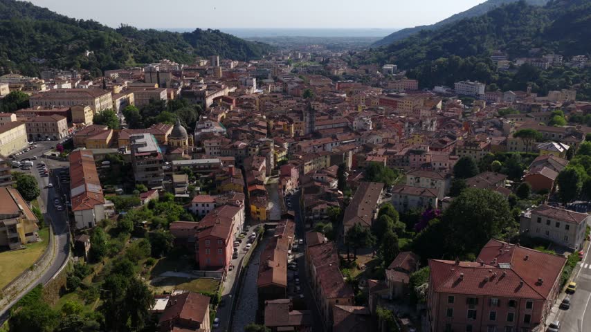 Aerial view of the historic town of Carrara nestled in the mountains of Tuscany, featuring terracotta rooftops, narrow streets, and lush green hills in Carrara, Tuscany, Italy.