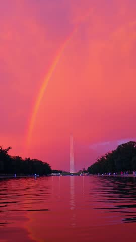 Rainbow above the Washington Monument and Reflecting Pool in Washington DC. A rainbow arcs over the distant obelisk beneath pink clouds reflected in rippling water between trees.