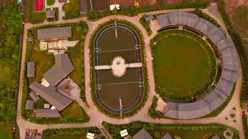 Aerial view of a modern resort complex featuring a central oval pool and a large circular lawn surrounded by landscaped gardens in Surat, Gujarat, India.