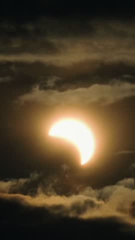 The partial solar eclipse of August 12, 2026, showing the moon passing in front of the sun, creating a spectacular celestial event in a dramatic and cloudy sky with a golden glow