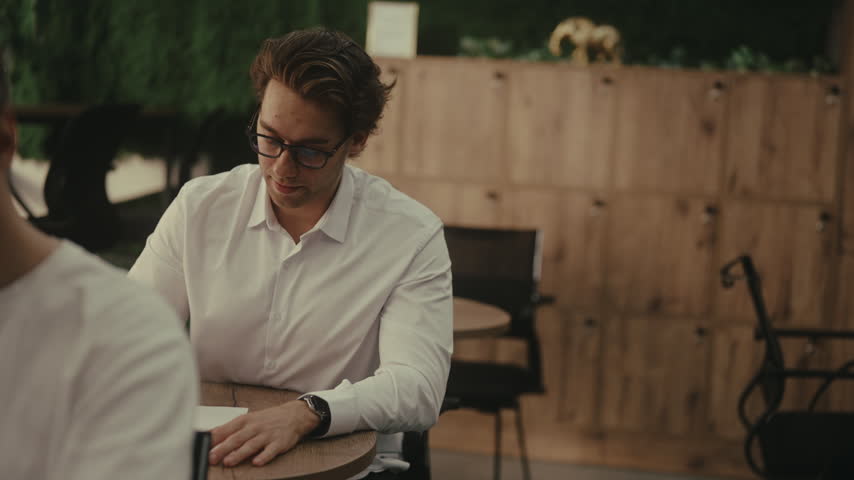 Two male students sitting at table during difficult university exam, one person struggling and asking classmate for help, who discreetly showing answers on paper. Shooting in slow motion.