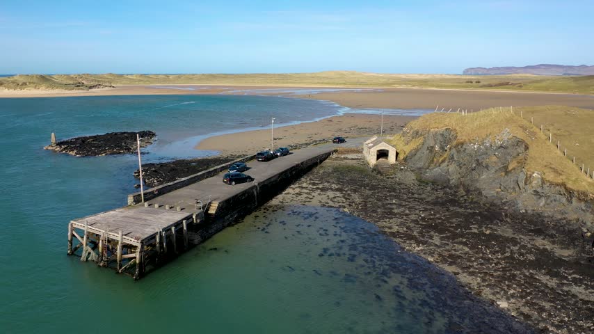 Aerial view of the historic stone pier at Portnablagh with parked cars and a small stone building on the rocky coastline in Portnablagh, County Donegal, Ireland.