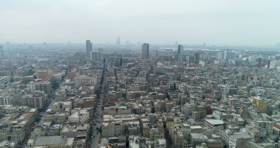 Aerial view of the dense urban cityscape of Karachi, featuring numerous residential and commercial buildings, narrow streets, and a hazy sky in Karachi, Sindh, Pakistan.
