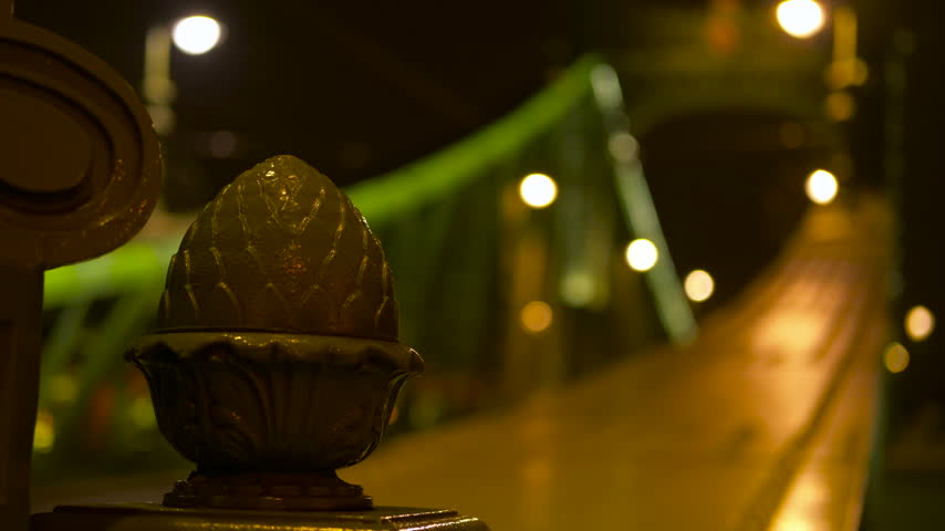 Ornate metal detail on the liberty bridge at night in budapest. Close-up of an ornate metal decoration on the liberty bridge in budapest, hungary, with defocused traffic and city lights