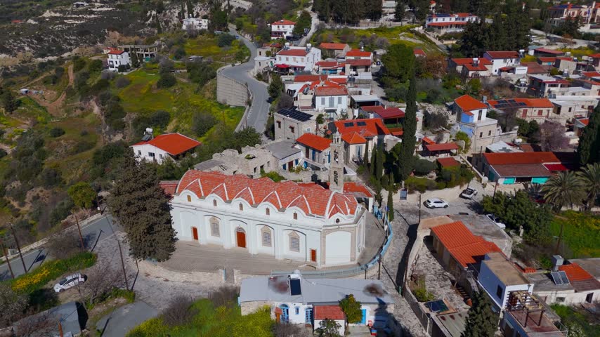 A drone descends toward the historic stone architecture of the Saint Charalambos Orthodox Church in the traditional village of Kato Drys, Cyprus.