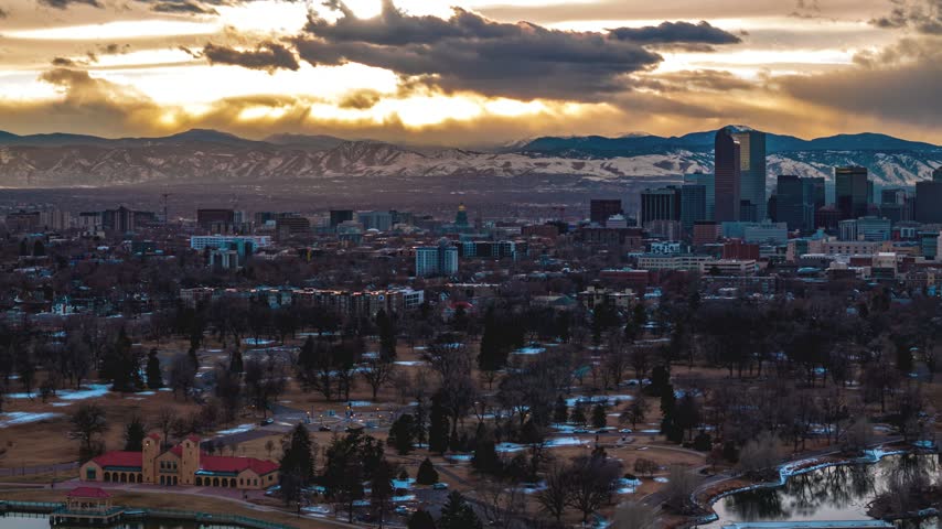Aerial view of Denver skyline with Rocky Mountains in the background under a dramatic sunset sky in Denver, Colorado, United States.