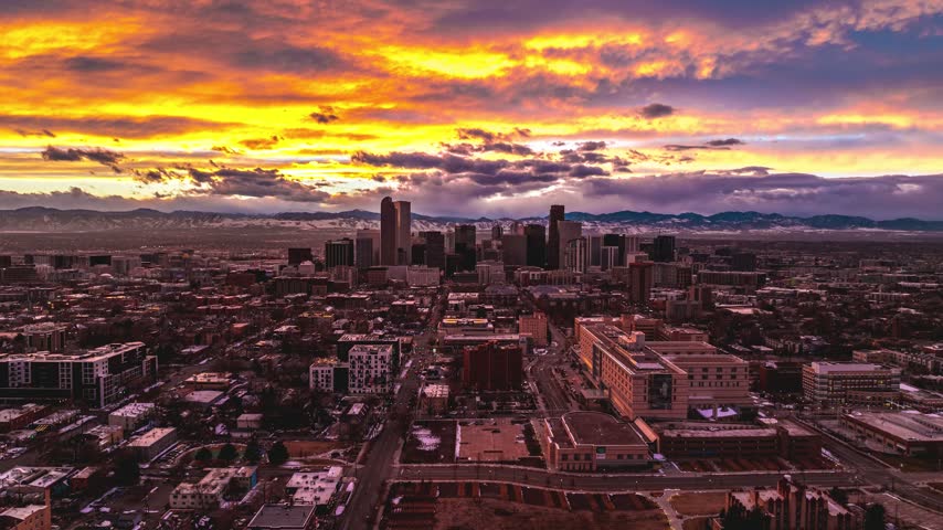 Aerial view of the Denver skyline illuminated by a vibrant sunset with dramatic clouds over the city buildings and distant mountains in Denver, Colorado, United States.
