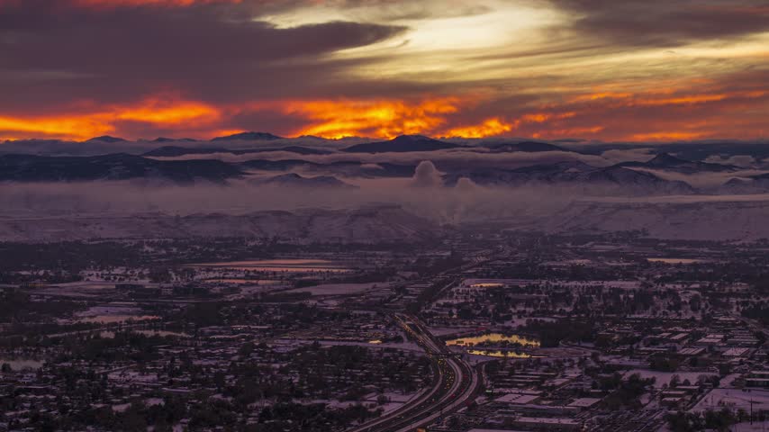 Aerial view of the city of Denver at sunset with the Rocky Mountains in the background and a highway winding through the urban landscape in Denver, Colorado, United States.