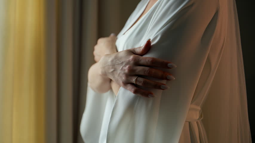 Close up of a bride in an elegant white wedding dress gently holding her arm while getting ready for the wedding ceremony.
