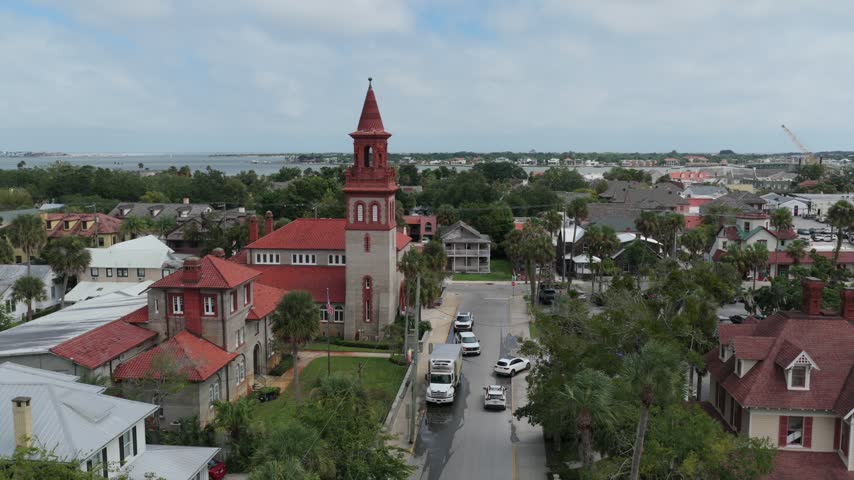 Aerial view of Grace United Methodist Church with its distinctive red roof and tower, surrounded by historic buildings and palm trees in St. Augustine, Florida, United States.