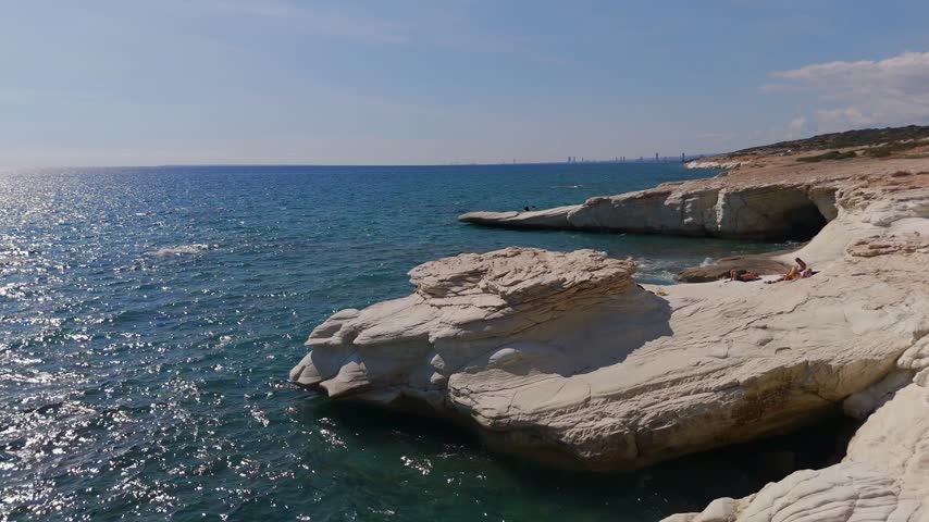 A low-altitude drone shot tracking over unique white chalk rock formations with people sunbathing along the Mediterranean coast in Limassol, Cyprus.