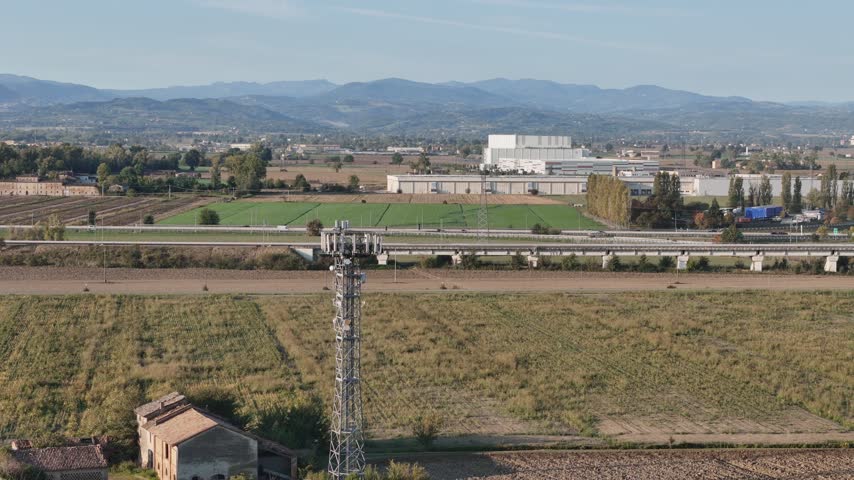 Aerial view of a telecommunications tower near the A1 and A21 motorways, with the Arda service area and surrounding agricultural fields in Fiorenzuola d