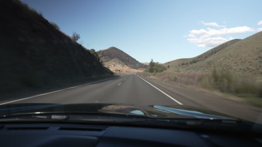 Driving POV through dry rolling hills on a highway in Central Oregon