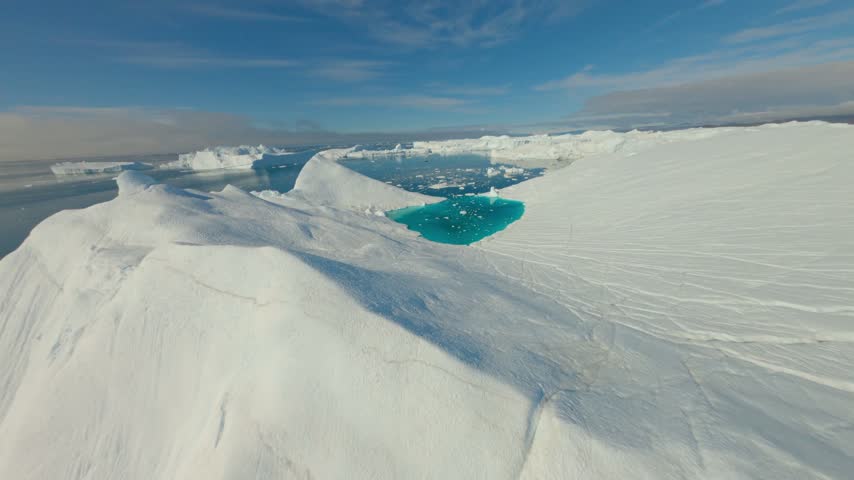 FPV aerial view of a turquoise meltwater pool on a massive iceberg in the arctic landscape Ilulissat, Avannaata, Greenland.