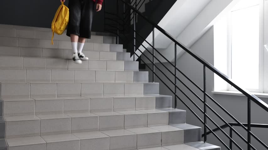 Stressed teenage boy with backpack sitting on stairs indoors. Camera moving forward