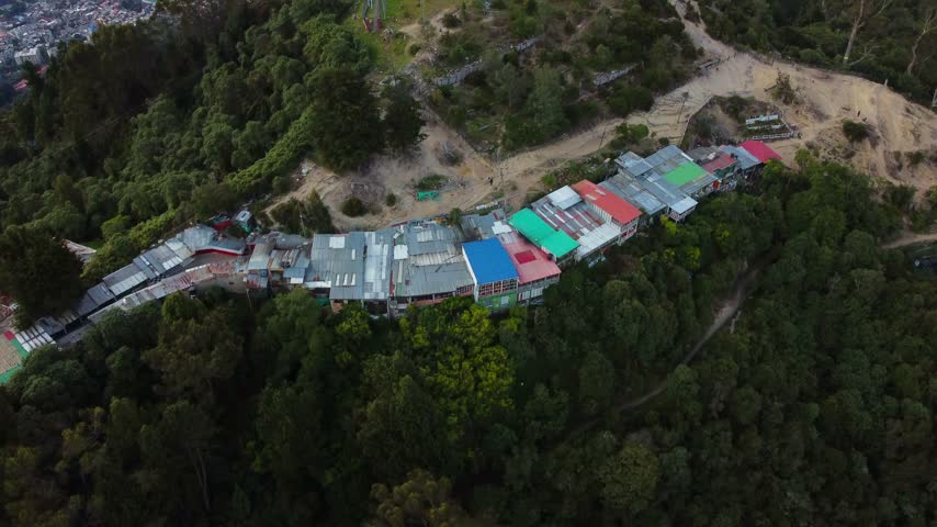 Drone footage of tall red-and-white telecommunication towers on a forested mountain summit near Monserrate, overlooking the city of Bogota, Colombia