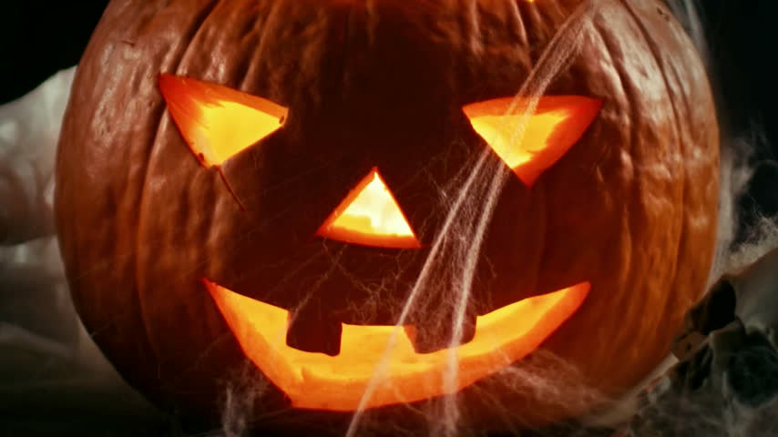 Glowing carved pumpkin surrounded by spider webs for Halloween decoration and seasonal content