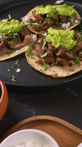 Gourmet beef tacos topped with green guacamole and fresh herbs on dark background