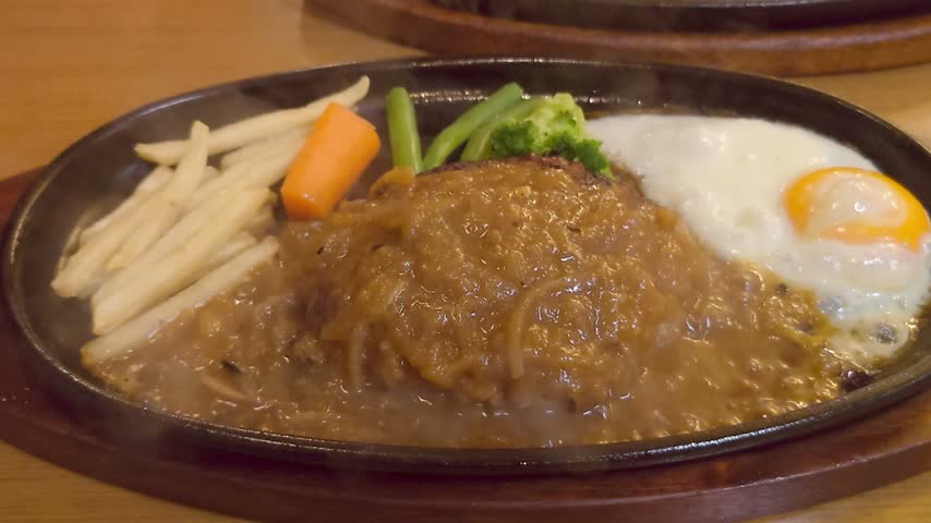 Sizzling hamburger steak with fried egg on hot iron plate with steam and sauce
