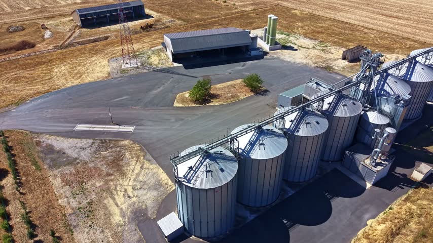 Long row of large metal grain silos and agricultural storage facilities surrounded by farm fields
