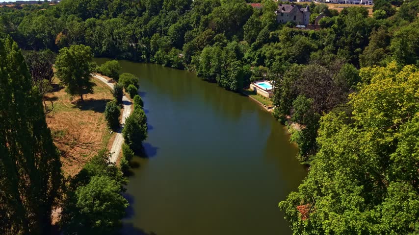 Mayenne River past residential house with outdoor swimming pool surrounded by green trees in Changé, France. Aerial drone