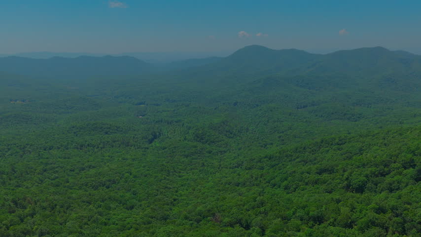 Aerial view of layered Appalachian mountain ridges fading into blue summer haze above a vast unbroken hardwood forest in rural Virginia under a clear blue sky.
