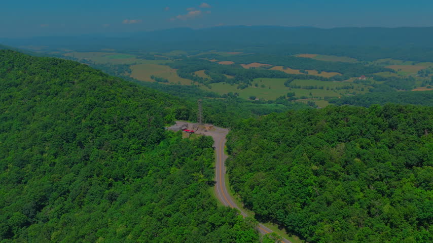 Aerial of a rustic country store and roadside attraction on a forested Virginia mountaintop, with red awnings, parked motorcycles, a steel observation tower and hazy Appalachian valley behind.