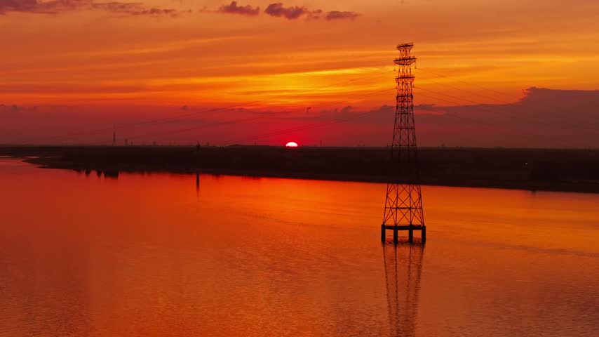 Telephoto view captures orange sunset behind a power tower on the Daugava