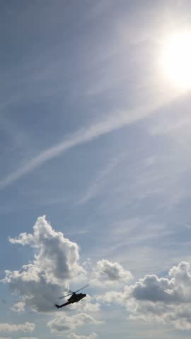Vertical screen military helicopter flies beneath bright sun and dramatic clouds during aerial demonstration showing dynamic aviation motion and powerful rotorcraft aloft