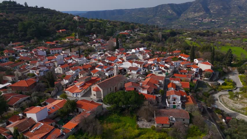 A drone orbit shot of a traditional stone Orthodox church located in the historic mountain village of Laneia, Cyprus. The footage shows the architectural details and surrounding rooftops on a clear winter day.
