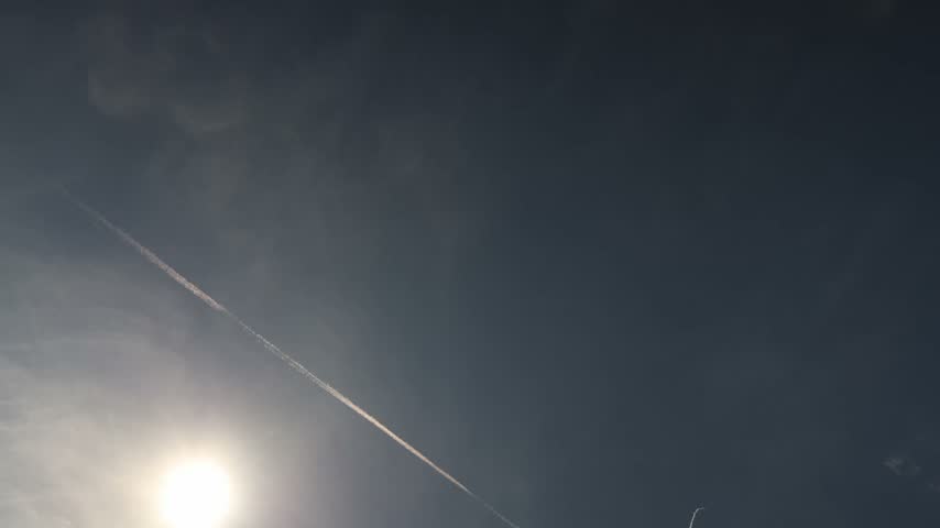Fighter jet crosses the bright sky leaving a long white contrail above the glowing sun while dramatic clouds create a striking aviation scene high in the atmosphere aloft