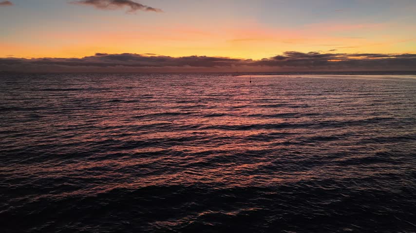 Aerial moving forward from Point Venus over rippling water, revealing the golden sunset horizon and dark coast of Tahiti island at twilight