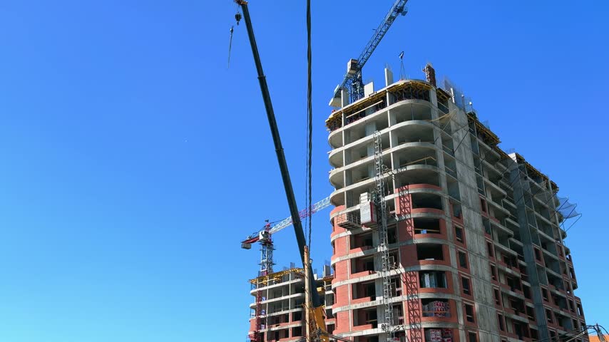 High-rise residential building under construction with elevator rising and tower crane against clear blue summer sky