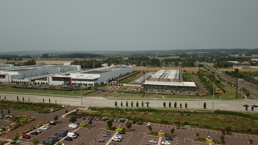 View of large data center complexes in Hillsboro, Oregon, featuring industrial buildings and rooftop cooling systems supporting cloud computing, AI, and digital infrastructure. Wide drone orbit.