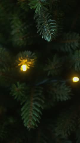 Vertical video. Woman decorating Christmas tree with Christmas ornaments.