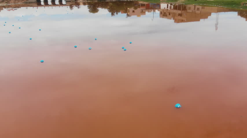 Drone flies over a lake reflecting the sky with small floating spheres, Morocco