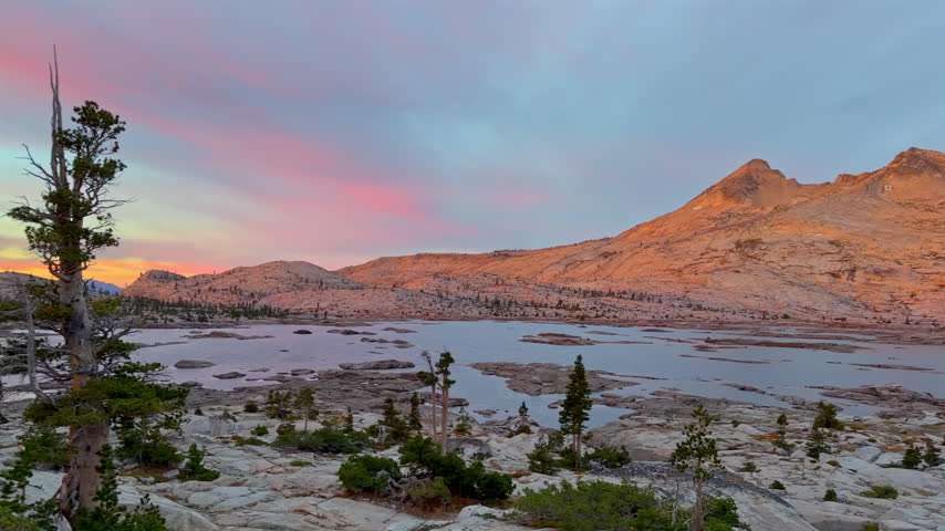 Warm dawn light colors granite mountains and clouds above Lake Aloha and scattered pines in Desolation Wilderness, Sierra Nevada, California, United States.