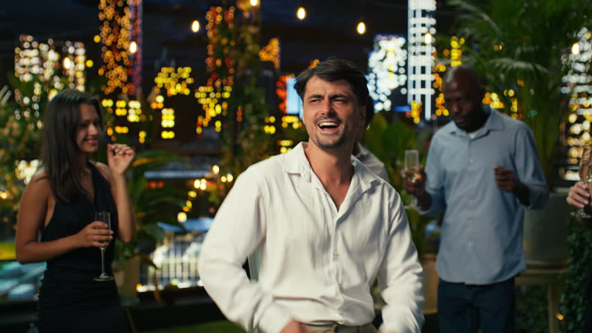 Thrilled man cheering and dancing at anniversary party, surrounded by partygoers while confident guest energizes surrounding crowd with his dance moves in lively outdoor setting