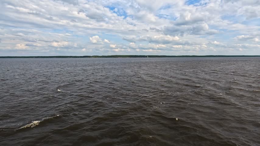 A wide dark lake stretches under a dramatic sky filled with heavy swirling clouds. Dramatic natural landscape.