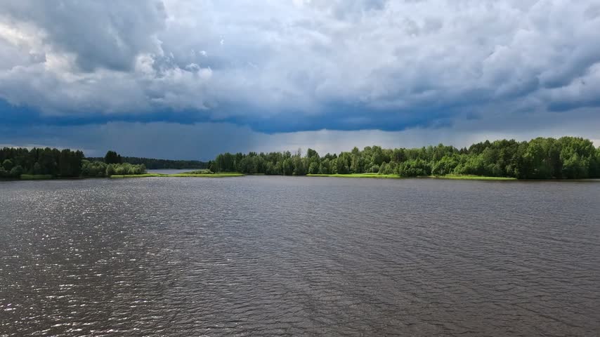 A wide dark lake stretches under a dramatic sky filled with heavy swirling clouds. Dramatic natural landscape.