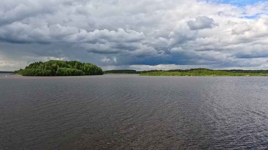 A wide dark lake stretches under a dramatic sky filled with heavy swirling clouds. Dramatic natural landscape.