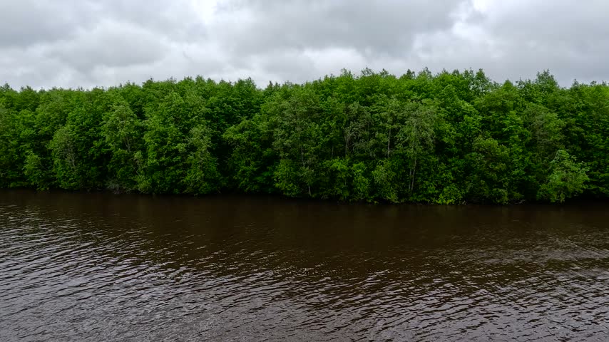 A wide dark lake stretches under a dramatic sky filled with heavy swirling clouds. Dramatic natural landscape.