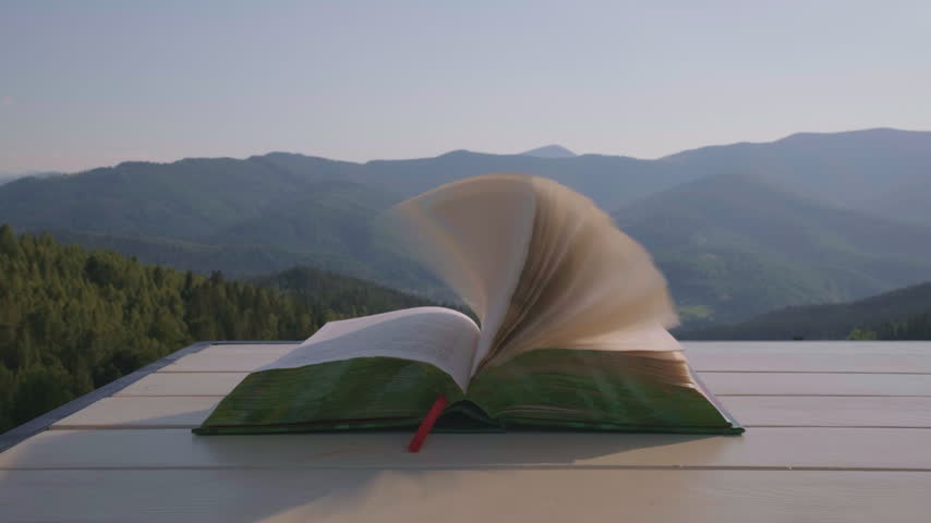 Open Book Pages Flipping in Wind on Table Against Mountain Landscape