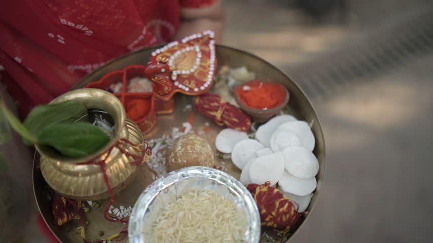Person hold metal tray with ritual items, metal pot, raw rice, red powder, sweets, and worship elements for cultural ceremony, prayer, and festival celebration with spiritual mood