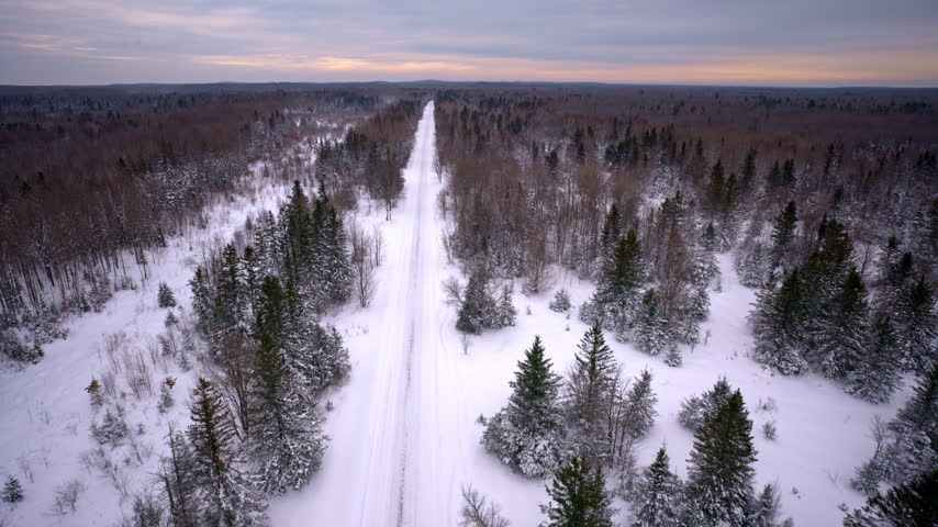Aerial shot of a snow-covered road traveling through Northern Michigan wilderness