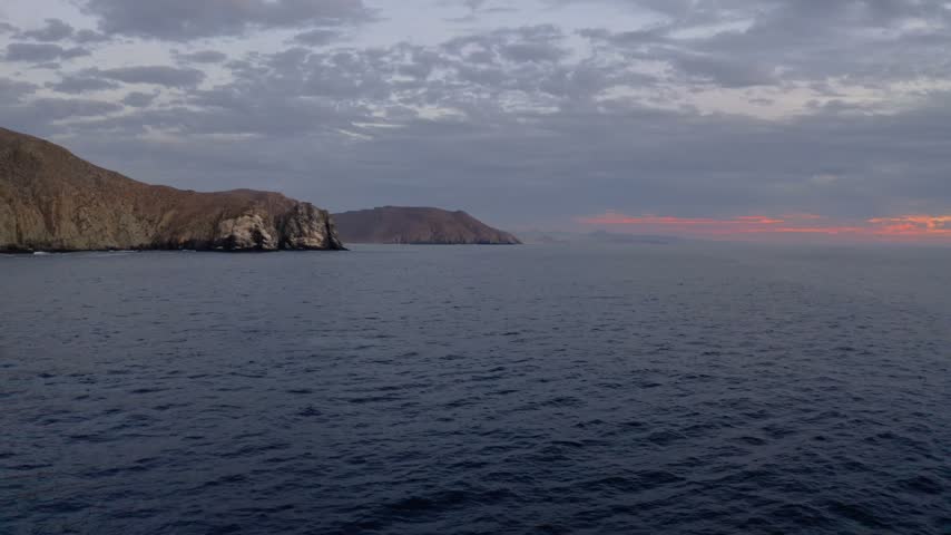 Scenic aerial footage of a wild whale jumping out of the water near dramatic desert mountains and coastline during a beautiful dusk.