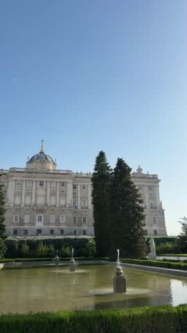 Famous Royal Palace of Madrid seen from the Sabatini Gardens on a sunny day with fountains and clear blue sky, a well-known tourist attraction and historical landmark in Spain