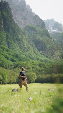 Female hiker taking photos with a professional camera while exploring a scenic forest with mountain views, combining hiking, travel and nature photography.